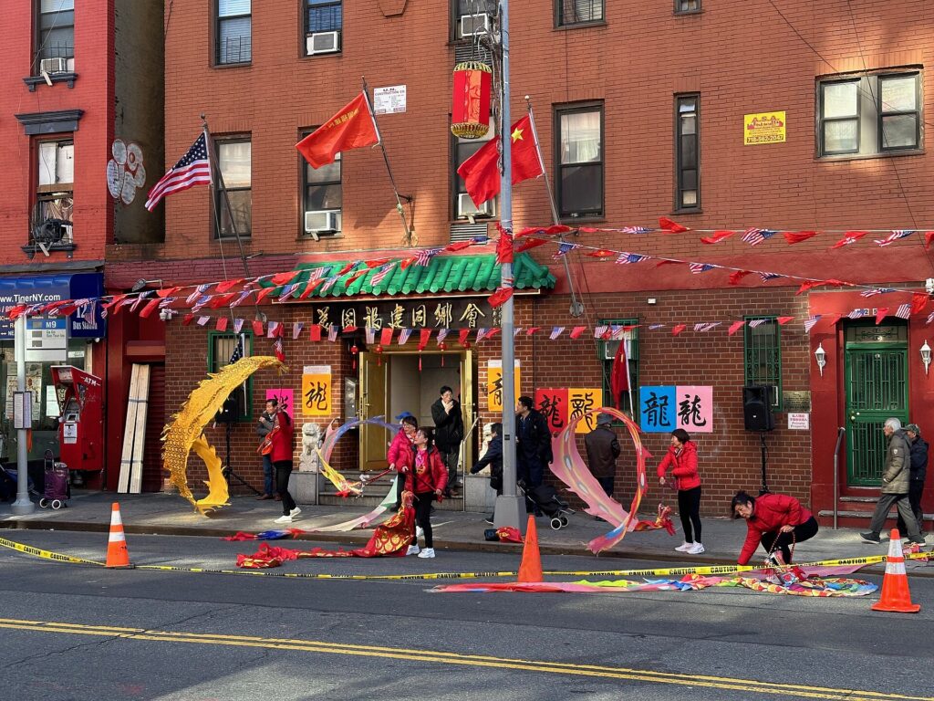 outside of the mutual aid building in Chinatown, dancers move dragons on poles to celebrate the new year