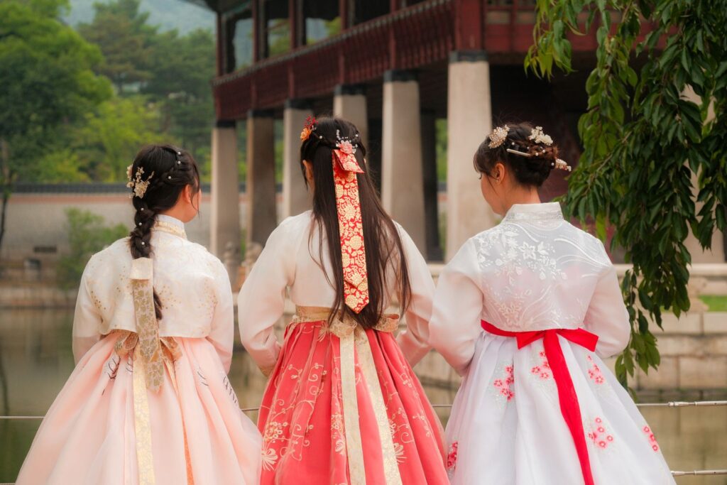 Three female friends wearing colorful hanbok explore a serene traditional setting.